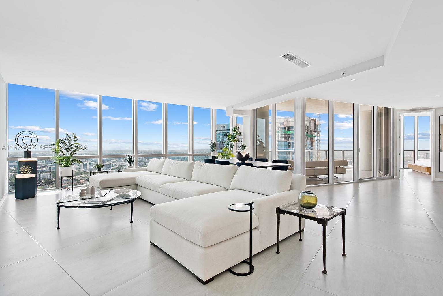 A modern, open-concept living room features a white sectional sofa, floor-to-ceiling windows, and tile flooring — 851 NE 1st Ave # 5402, Miami FL 33132, MIAMI, FL