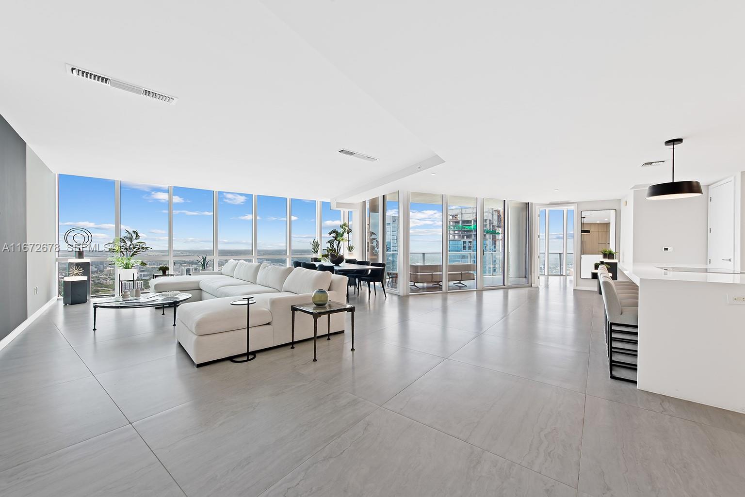 A spacious, modern open-concept living area features floor-to-ceiling windows, light tile flooring, and white furniture — 851 NE 1st Ave # 5402, Miami FL 33132, MIAMI, FL