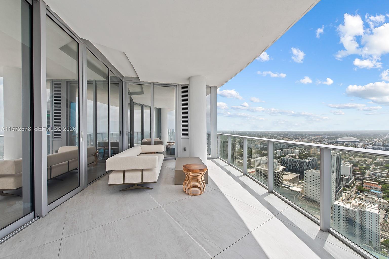 A modern high-rise balcony features a white sofa, a small wooden table, and city views — 851 NE 1st Ave # 5402, Miami FL 33132, MIAMI, FL