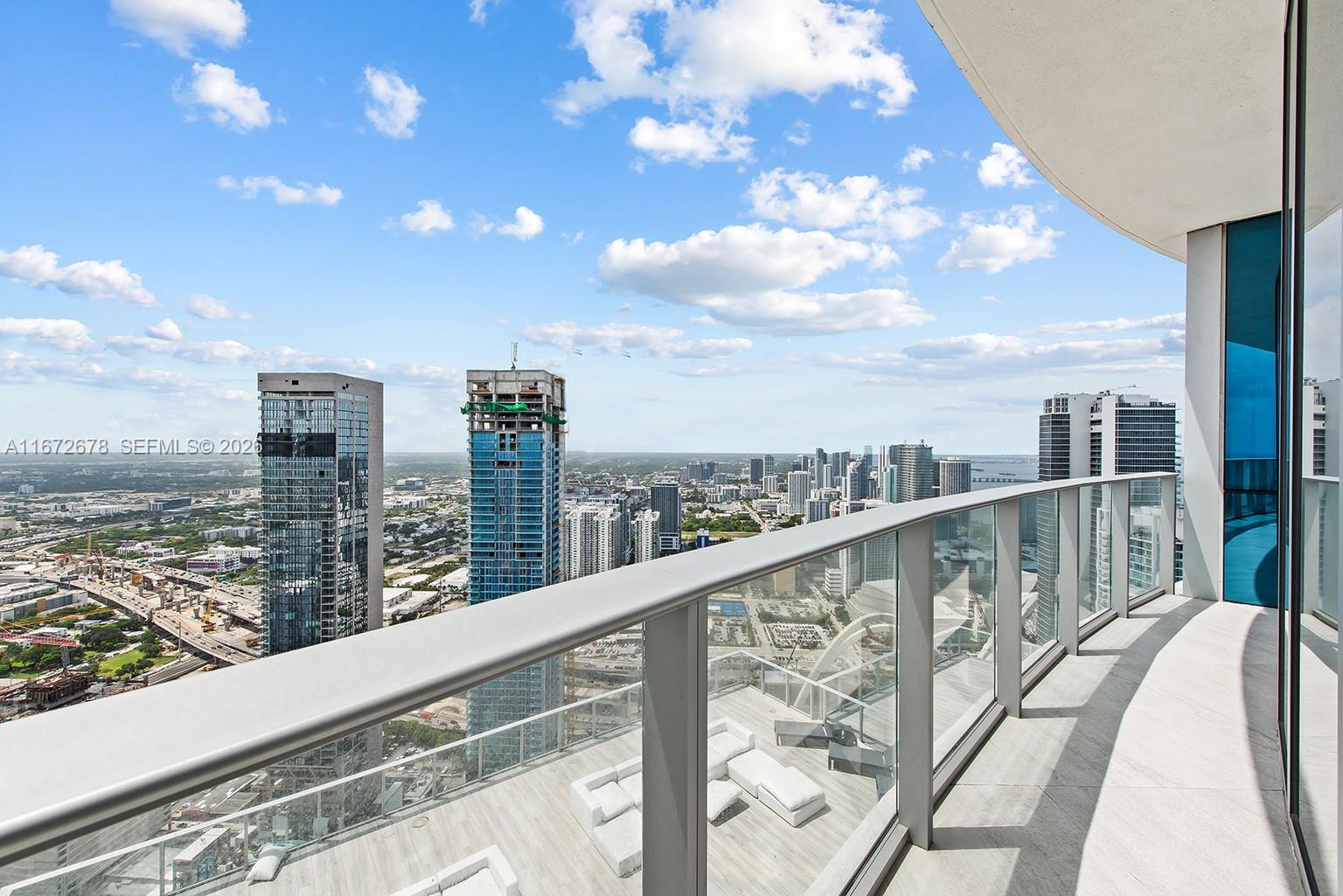 A high-rise balcony with glass railings overlooks a city skyline under a blue sky — 851 NE 1st Ave # 5402, Miami FL 33132, MIAMI, FL
