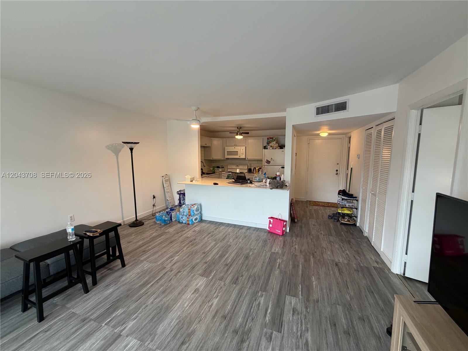 An open-concept living area features gray wood-look flooring, a kitchen island, and white walls — 4174 Inverrary Dr # 408, Lauderhill FL 33319, LAUDERHILL, FL