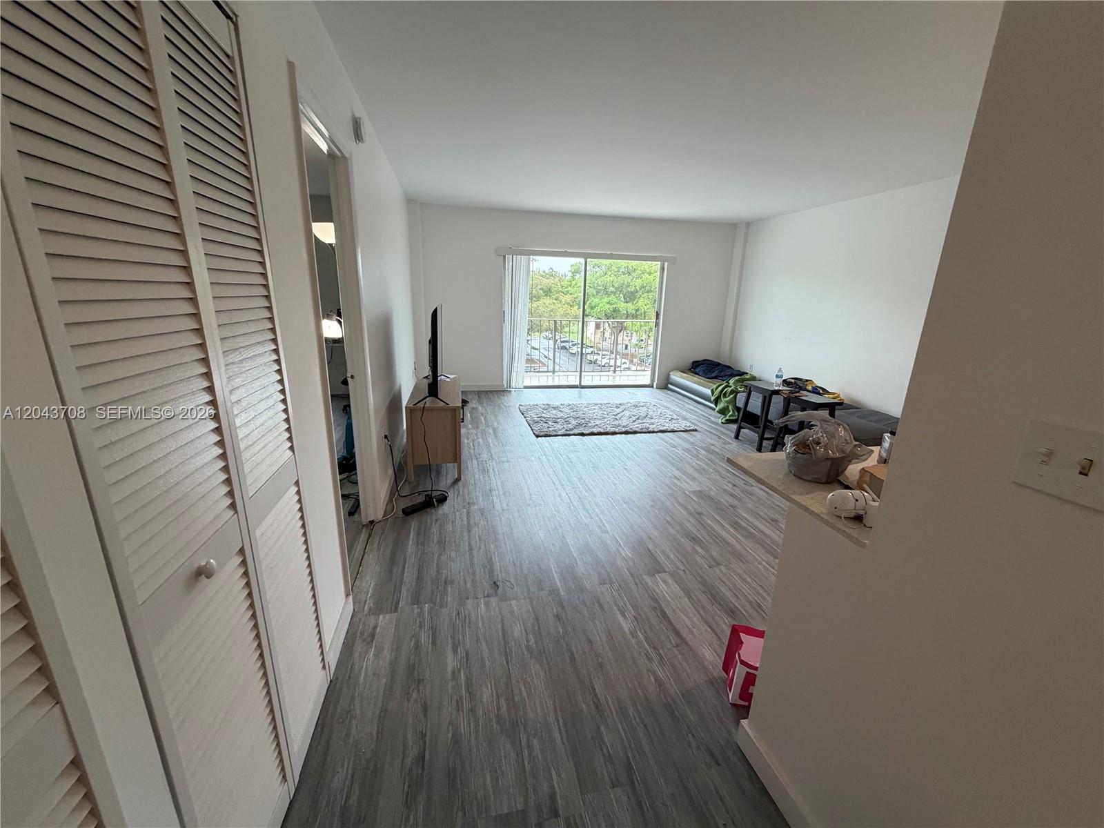 An open-concept living area features wood-look flooring, white walls, and a sliding glass balcony door — 4174 Inverrary Dr # 408, Lauderhill FL 33319, LAUDERHILL, FL