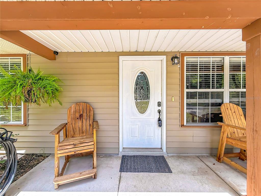 A covered front porch features two wooden rocking chairs, a white door, and a fern — 12290 SE 141ST AVENUE ROAD, OCKLAWAHA, FL