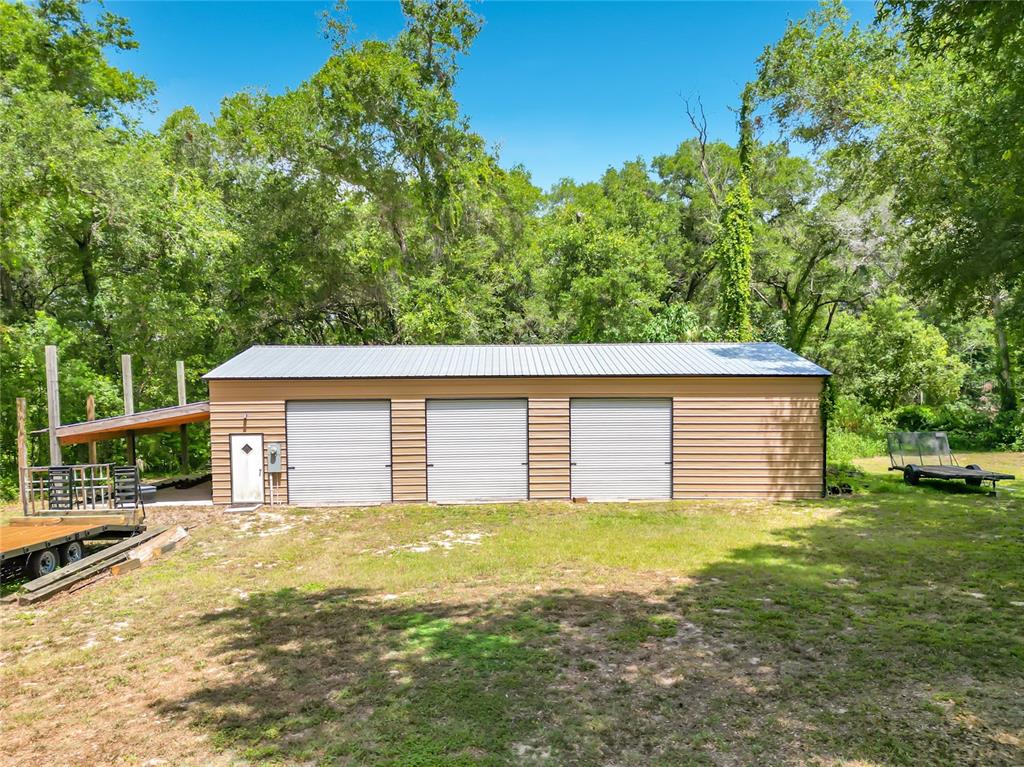 A detached three-bay metal garage sits on a grassy lot surrounded by dense trees — 12290 SE 141ST AVENUE ROAD, OCKLAWAHA, FL