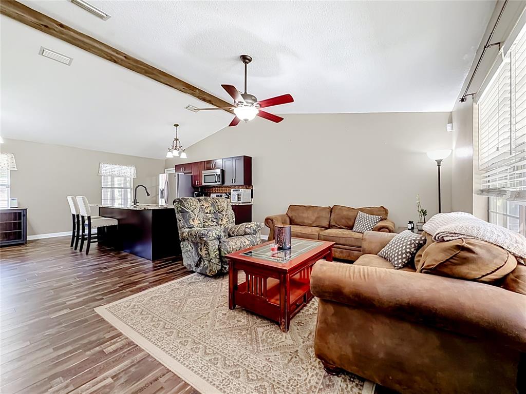 A living room with wood-look flooring, a vaulted ceiling, and an open kitchen area — 12290 SE 141ST AVENUE ROAD, OCKLAWAHA, FL
