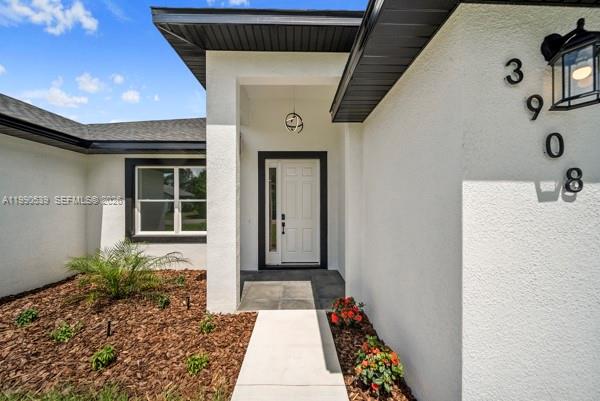 The exterior of a white house features a front door, a window, and a wall-mounted lamp — 3908 Garienda Ave, Sebring FL 33872, SEBRING, FL