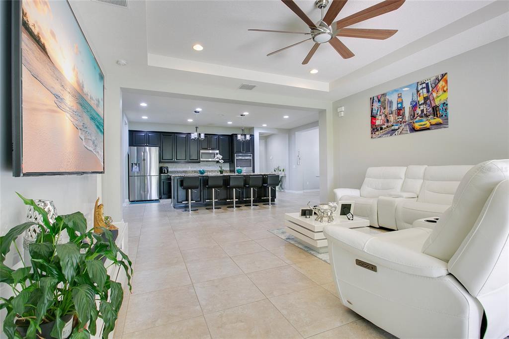 An open-concept living room features white leather furniture, tile flooring, and a dark kitchen island — 4918 WILDWOOD POINTE ROAD, WINTER GARDEN, FL