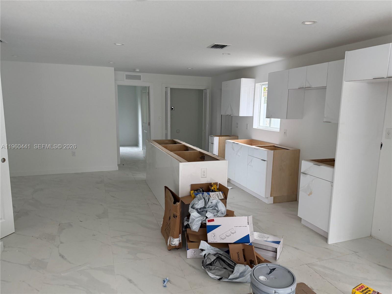 An unfinished kitchen features white cabinets, a central island, and light-colored marble-style tile flooring — 7823 NW 5th Ave, Miami FL 33150, MIAMI, FL