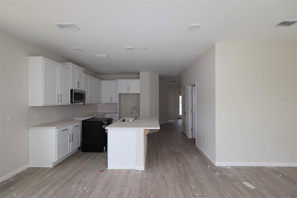 A modern kitchen features white cabinets, a central island with a sink, and light flooring — 1429 HYDE STREET, ST CLOUD, FL