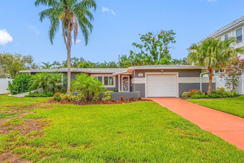 A single-story gray house features a white garage door, a palm tree, and a lawn — 328 BAYVIEW DRIVE NE, ST PETERSBURG, FL