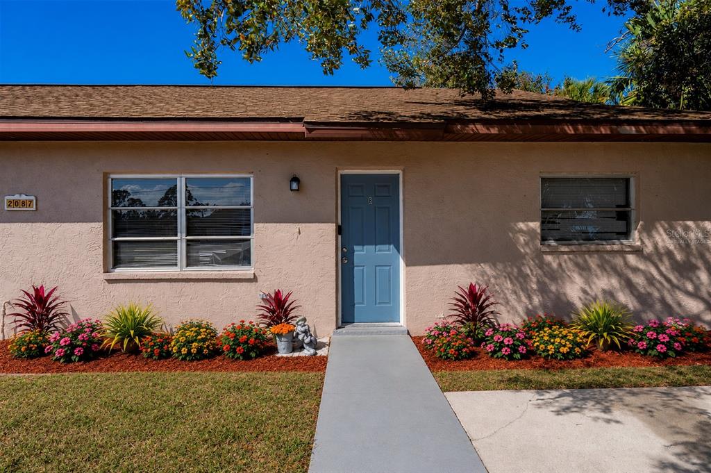 The exterior of a single-story house features a blue front door and landscaped flower beds — 2087 COMO STREET UNIT B, PORT CHARLOTTE, FL