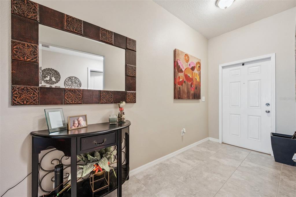 A foyer features a console table, a decorative mirror, floral wall art, and tiled flooring — 1615 REDMOND BROOK LANE, RUSKIN, FL