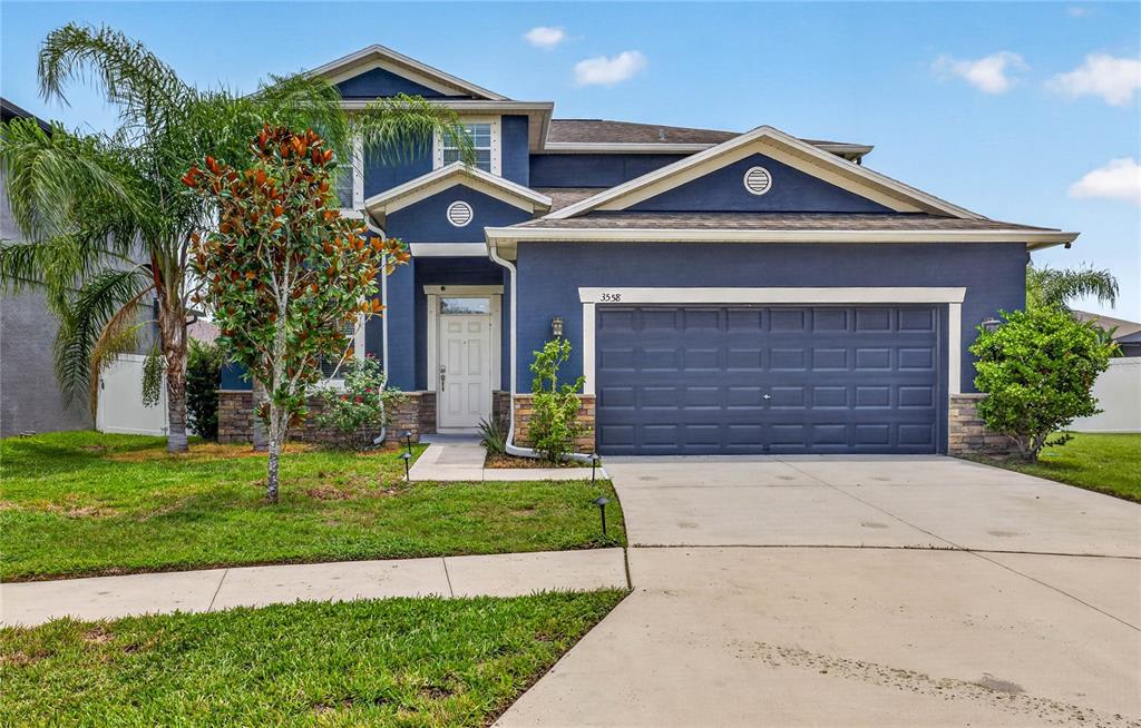 A two-story blue house features a two-car garage, stone accents, and a front palm tree — 3558 BRACKNELL COURT, LAND O LAKES, FL