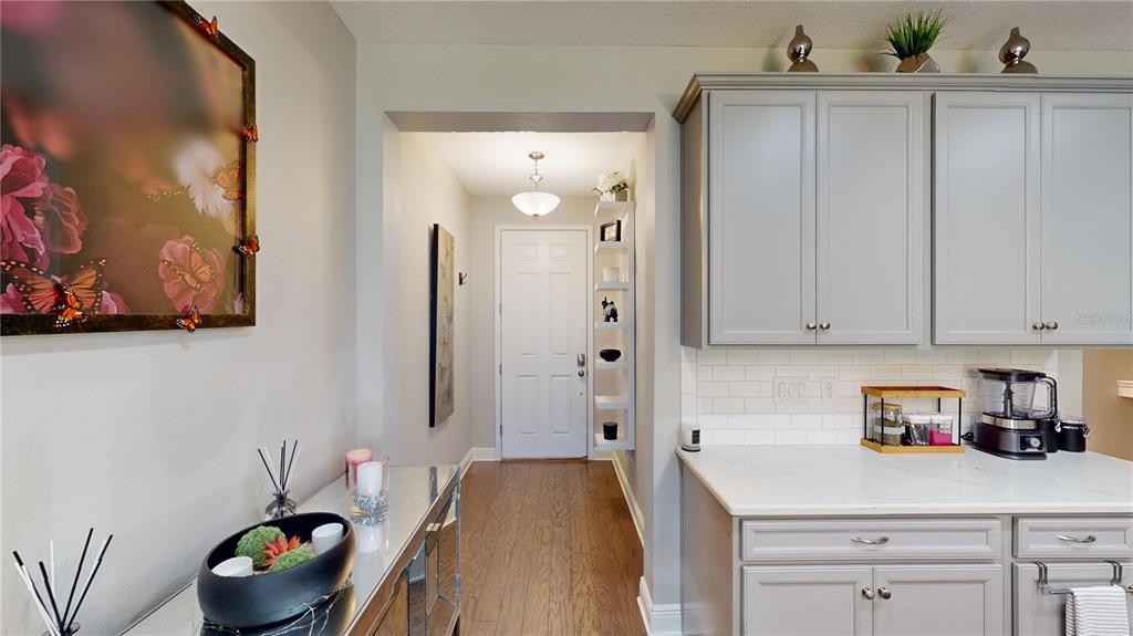 A kitchen with gray cabinets and white countertops leads into a hallway with a door — 14223 PONDHAWK LANE, TAMPA, FL