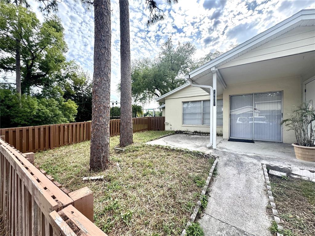 A concrete patio sits beside a house with a sliding glass door and wooden fence — 14607 PINE GLEN CIRCLE, LUTZ, FL