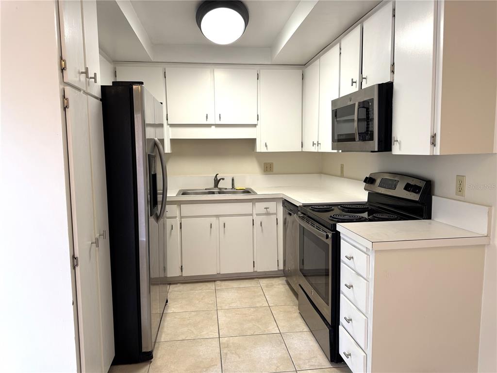 A kitchen features white cabinets, stainless steel appliances, a double sink, and tiled flooring — 14607 PINE GLEN CIRCLE, LUTZ, FL