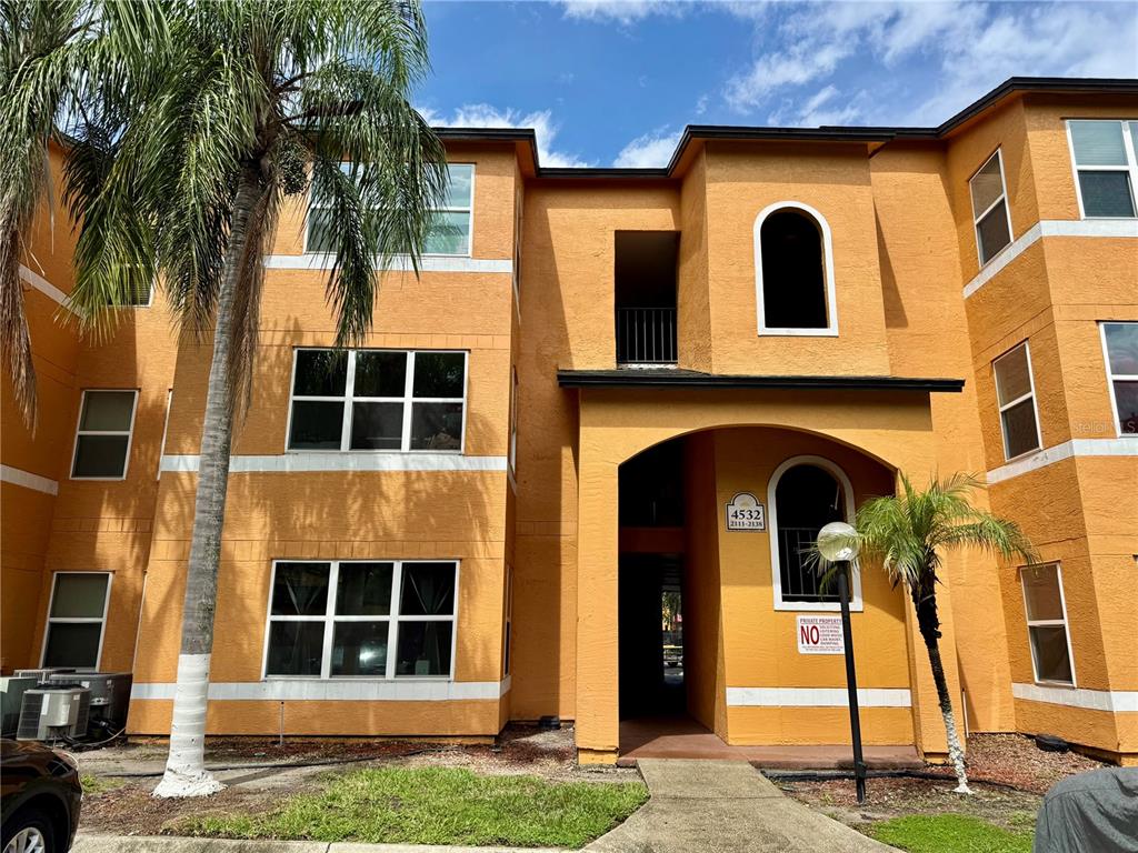 A three-story orange apartment building with a palm tree and a concrete walkway — 4532 COMMANDER DRIVE UNIT 2128, ORLANDO, FL