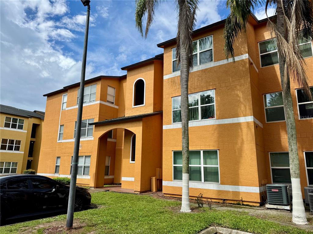 A three-story orange apartment building with white trim and palm trees in the foreground — 4532 COMMANDER DRIVE UNIT 2128, ORLANDO, FL
