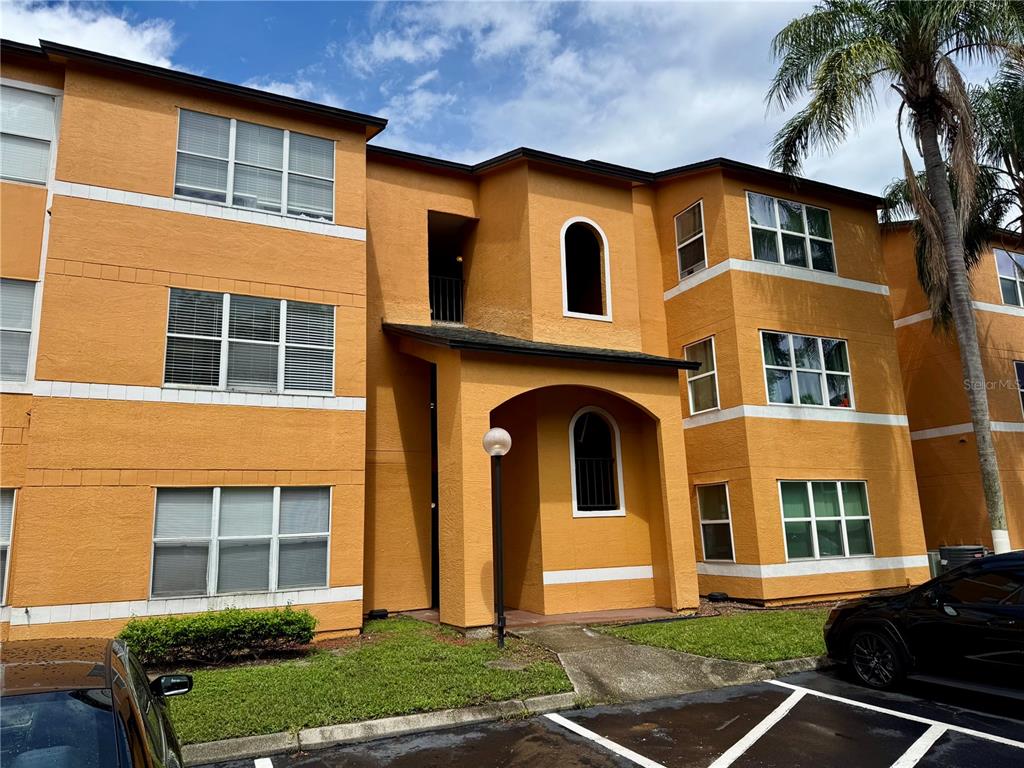 A three-story yellow apartment building with white trim and a parking lot in front — 4532 COMMANDER DRIVE UNIT 2128, ORLANDO, FL