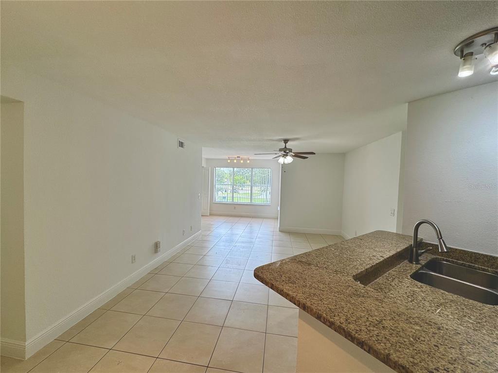 A kitchen counter with a granite top overlooks an open-concept living area with tiled floors — 4532 COMMANDER DRIVE UNIT 2128, ORLANDO, FL