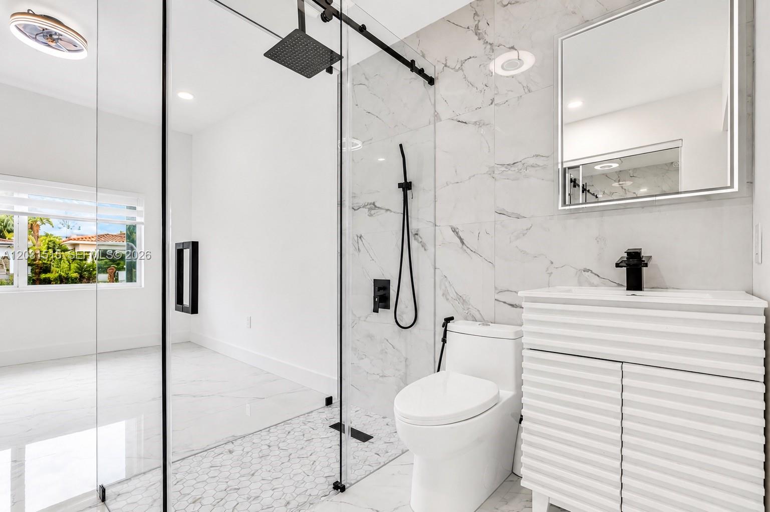 A modern bathroom features a glass-enclosed shower, marble-style tile walls, and a white vanity — 8819 Dickens Ave, Surfside FL 33154, SURFSIDE, FL