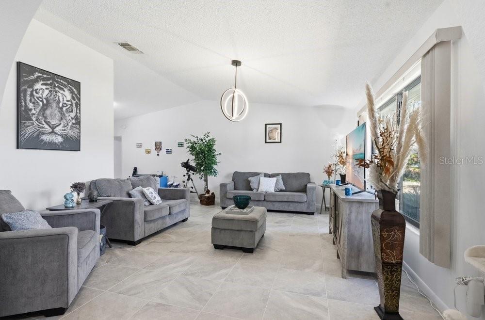 A living room features gray sofas, a matching ottoman, tile flooring, and a modern pendant light — 3270 DEER LICK COURT, KISSIMMEE, FL