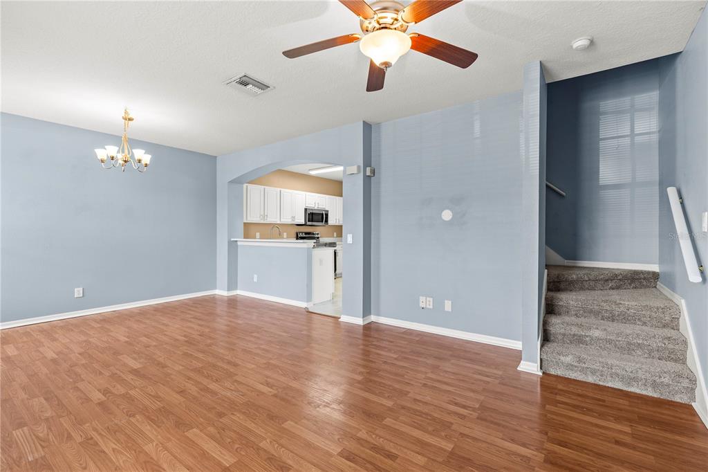 A living room with light blue walls, wood flooring, a ceiling fan, and adjacent stairs — 3423 SANTA RITA LANE, LAND O LAKES, FL