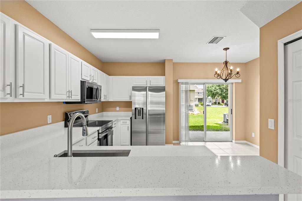 A kitchen with white cabinets, stainless steel appliances, and a dining area with sliding doors — 3423 SANTA RITA LANE, LAND O LAKES, FL