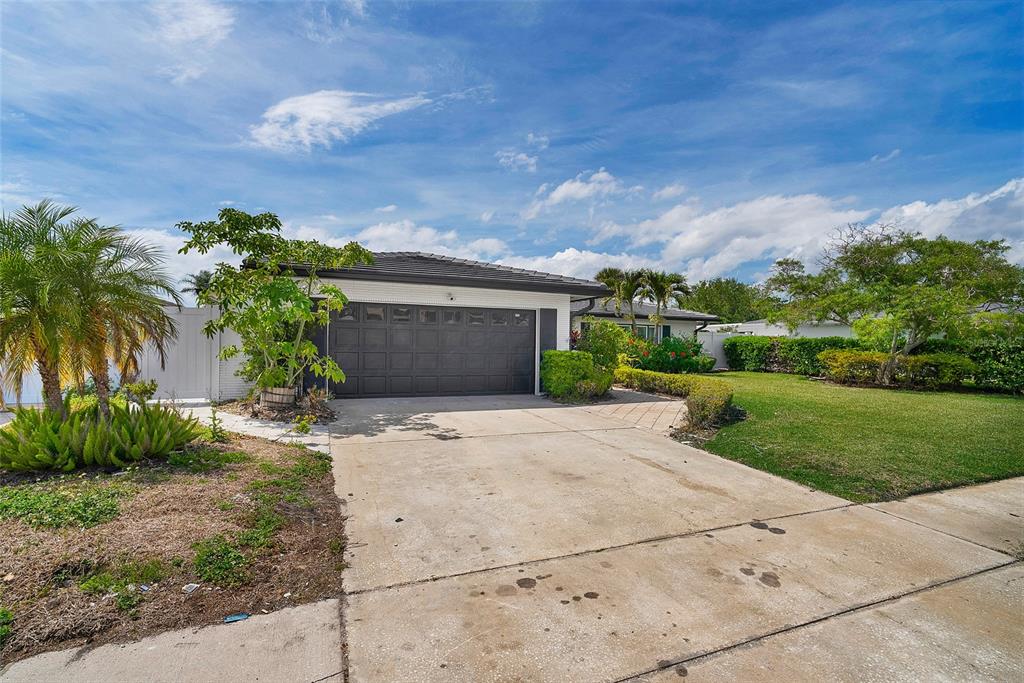 A single-story house with a dark garage door, concrete driveway, and surrounding landscaping — 3944 DORAL DRIVE, TAMPA, FL