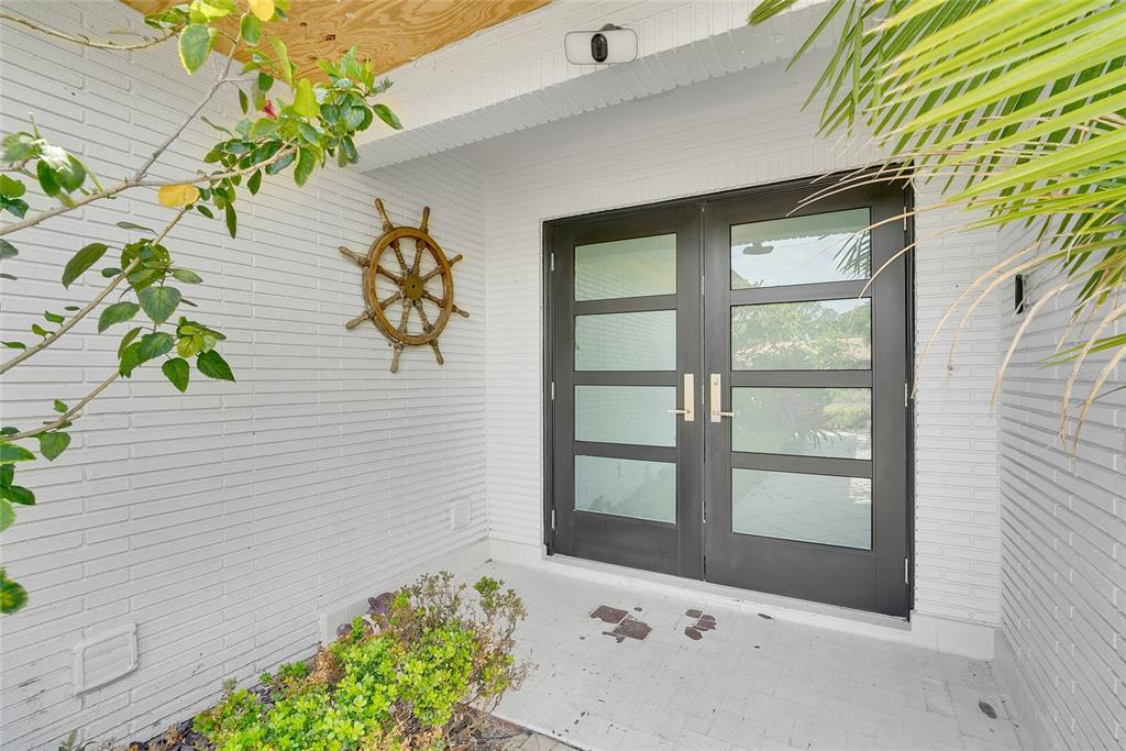 A white brick entryway features a dark double door with glass panels and a ship wheel — 3944 DORAL DRIVE, TAMPA, FL