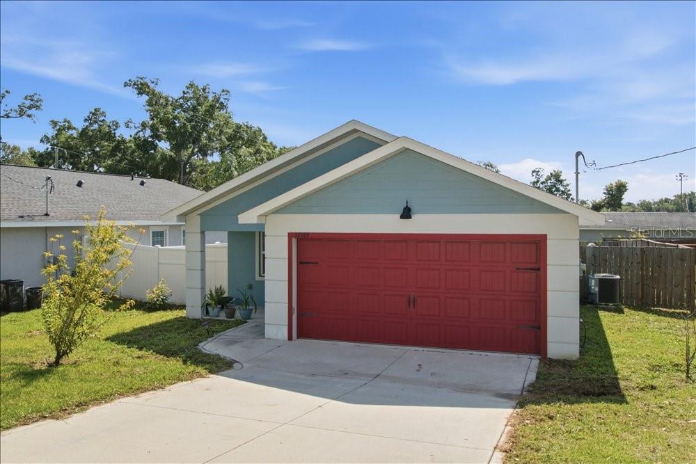 A single-story house features a red garage door, light blue siding, and a concrete driveway — 14584 20TH ST, DADE CITY, FL