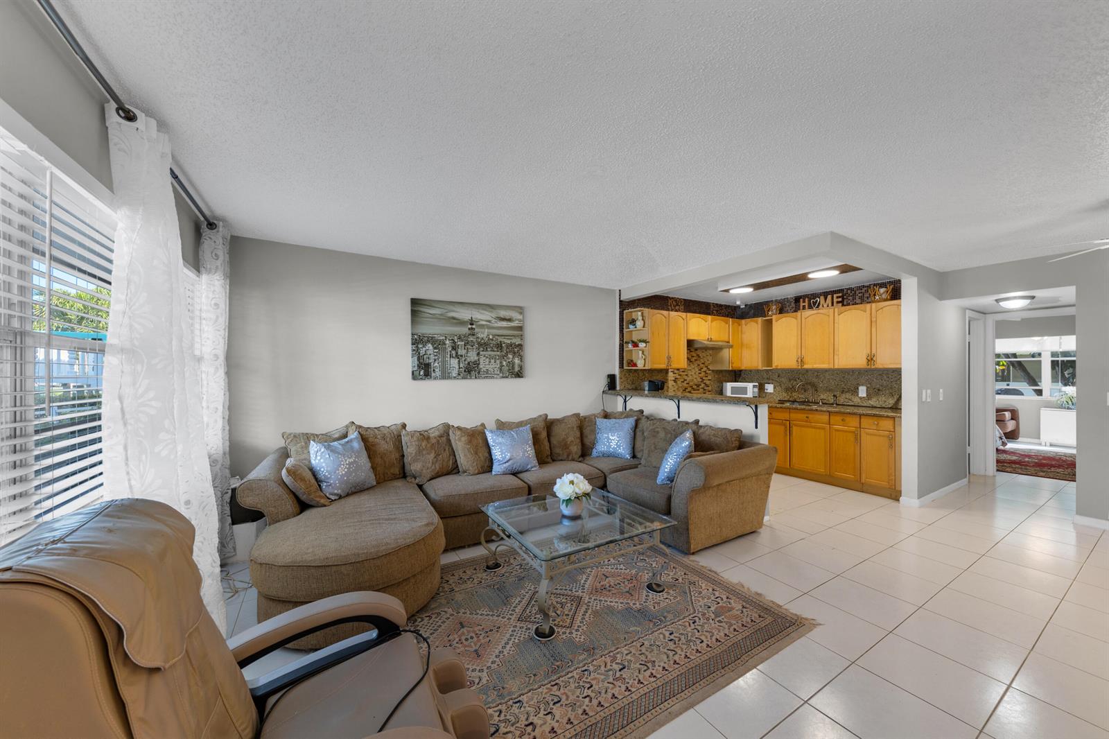 A living room with a sectional sofa and glass coffee table opens to a kitchen — 5 Newport A, Deerfield Beach FL 33442, DEERFIELD BEACH, FL
