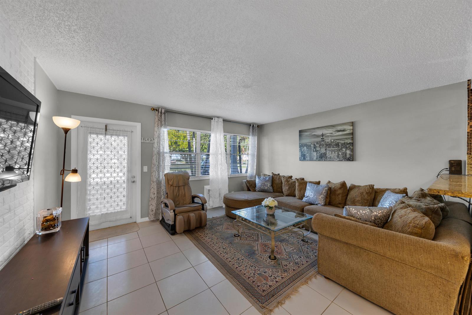 A living room features tile flooring, a large sectional sofa, a recliner, and a glass-topped table — 5 Newport A, Deerfield Beach FL 33442, DEERFIELD BEACH, FL