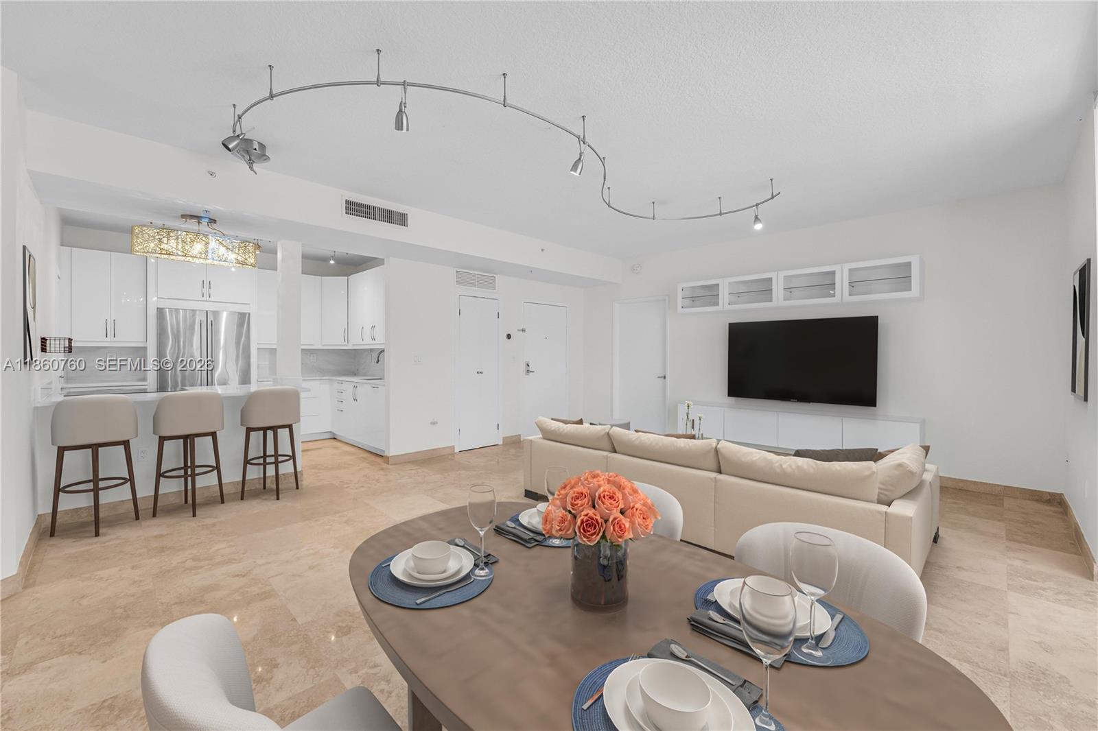An open-concept living and dining area features white cabinetry, tile flooring, and track lighting — 1 Century Ln # 202, Miami Beach FL 33139, MIAMI BEACH, FL