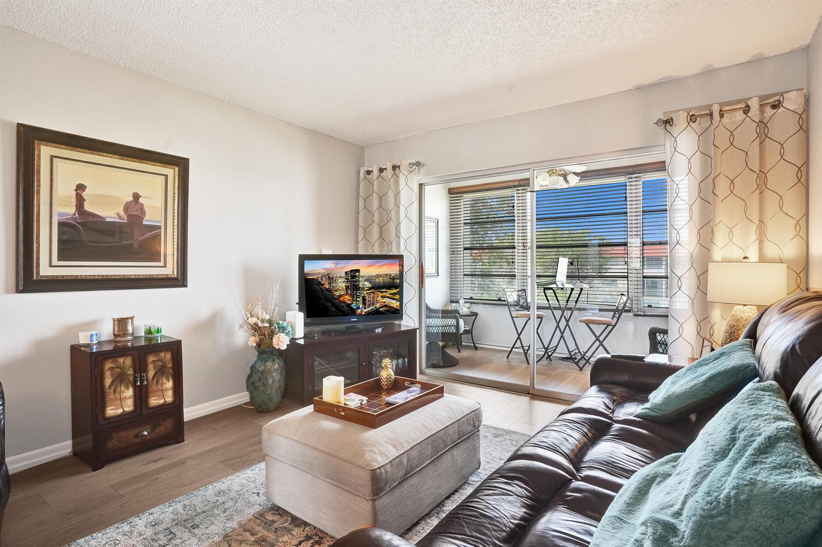 A living room features a leather sofa, an ottoman, a television, and a sliding glass door — 2901 E Sunrise Lakes Drive E # 305, Sunrise FL 33322, SUNRISE, FL