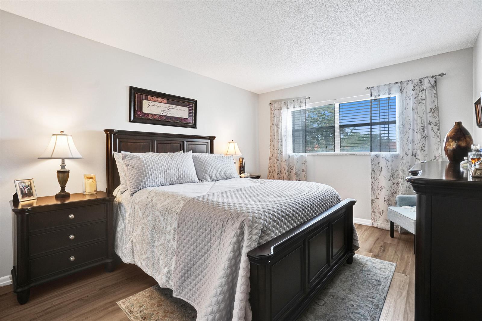 A bedroom features a dark wood bed frame, matching nightstand, and a window with curtains — 2901 E Sunrise Lakes Drive E # 305, Sunrise FL 33322, SUNRISE, FL