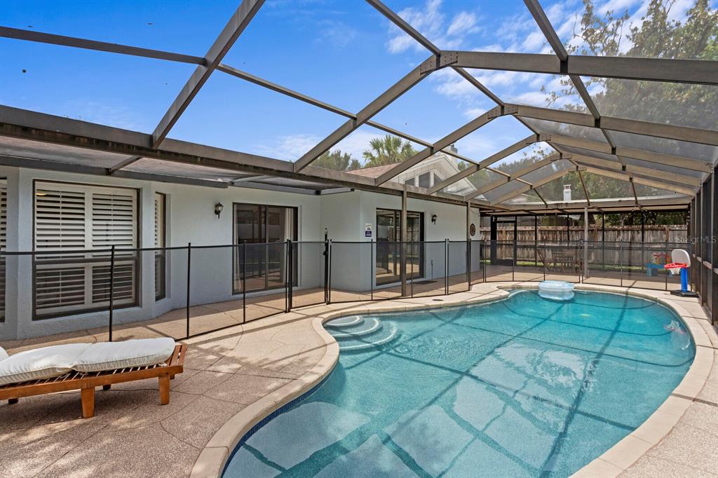 A screened-in patio features a swimming pool with a safety fence and lounge chair — 12803 RAIN FOREST STREET, TEMPLE TERRACE, FL
