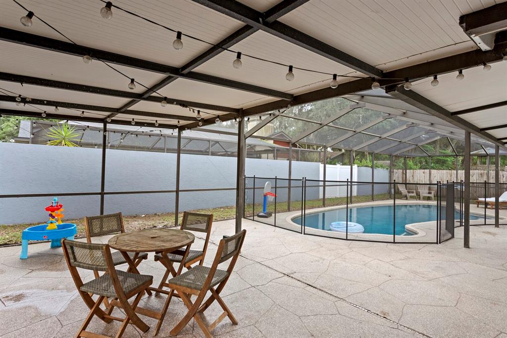 A covered patio features a dining set, a children's water table, and a fenced swimming pool — 12803 RAIN FOREST STREET, TEMPLE TERRACE, FL