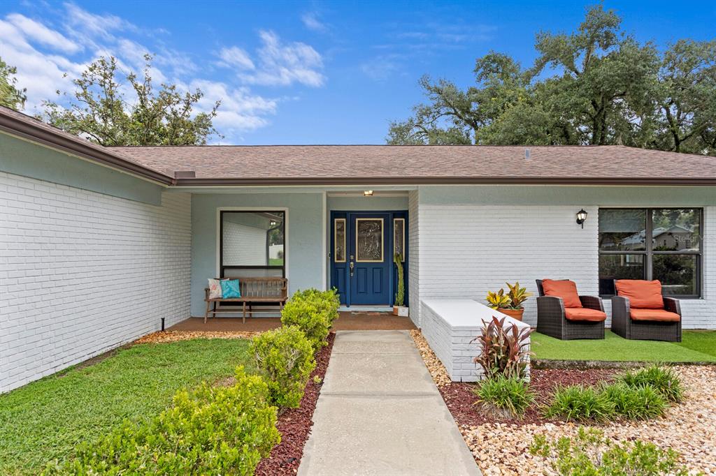 A single-story house with white brick walls, a blue front door, and a concrete walkway — 12803 RAIN FOREST STREET, TEMPLE TERRACE, FL