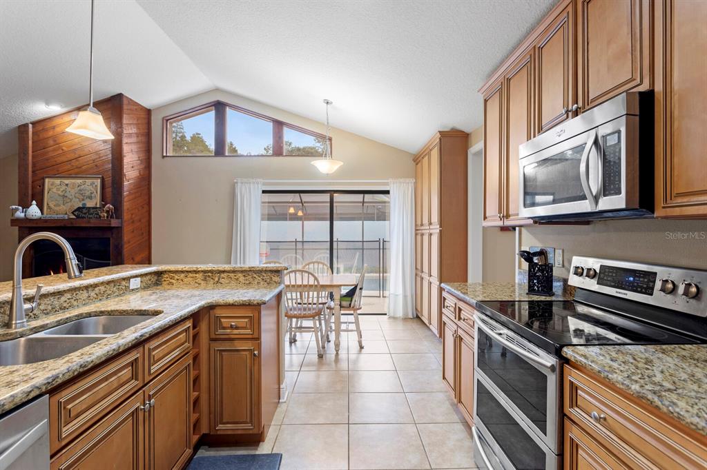 A kitchen with wood cabinets, granite countertops, and a dining area overlooking a screened patio — 12803 RAIN FOREST STREET, TEMPLE TERRACE, FL