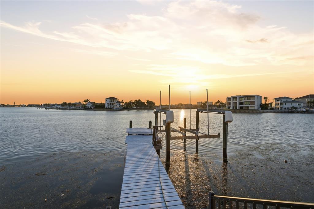 A wooden dock with a boat lift extends into a calm bay at sunset — 1818 DOLPHIN BOULEVARD S, ST PETERSBURG, FL