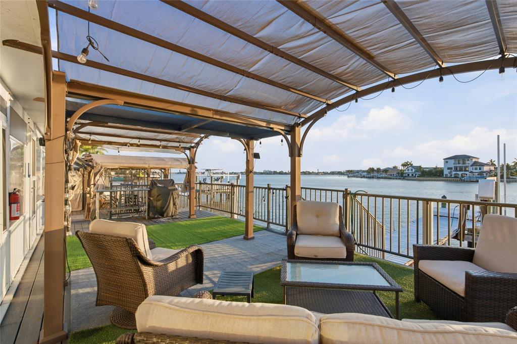 A covered outdoor patio features wicker furniture and artificial turf overlooking a waterfront view — 1818 DOLPHIN BOULEVARD S, ST PETERSBURG, FL