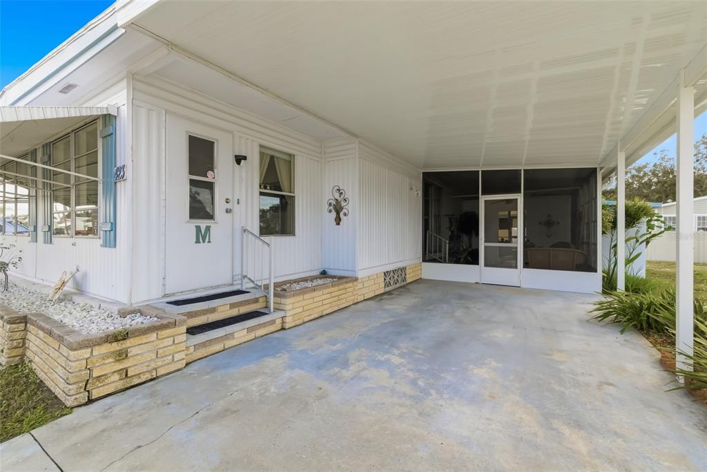 A white mobile home exterior features a concrete carport, a screened porch, and brick planters — 5619 BAYSHORE ROAD UNIT 423, PALMETTO, FL