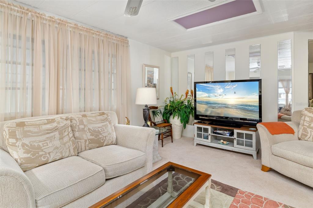 A living room features a beige sofa, a television on a stand, and mirrored wall panels — 5619 BAYSHORE ROAD UNIT 423, PALMETTO, FL