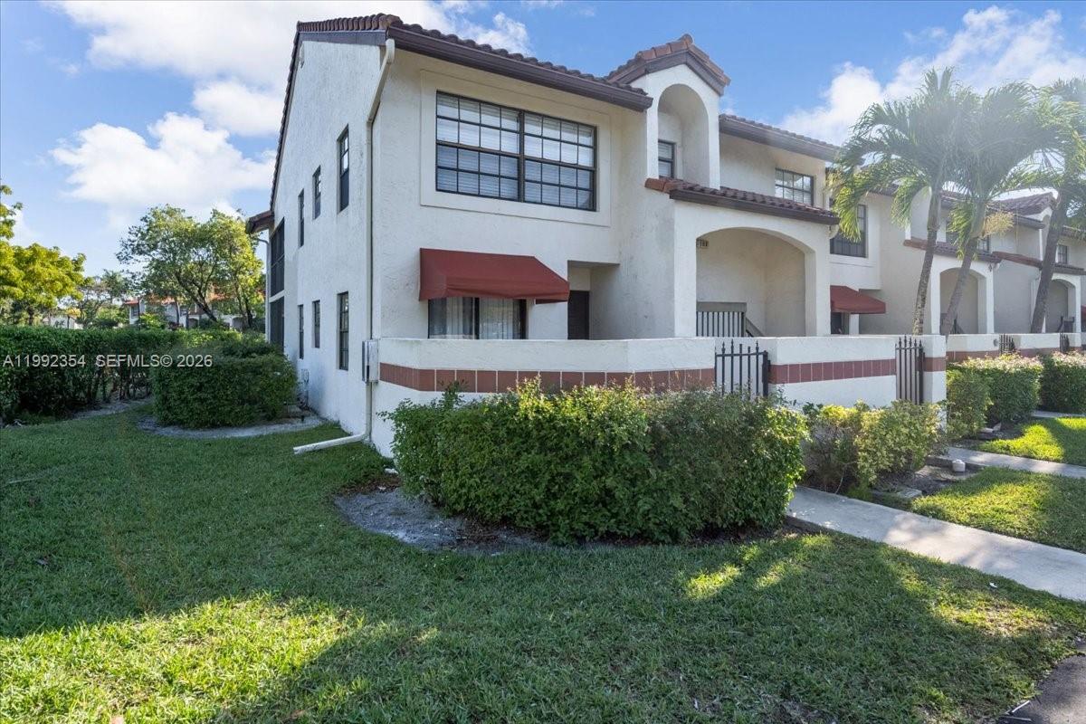 A two-story stucco townhouse features a red awning, arched entryway, and a fenced patio area — 101 Lincoln Ct # 101, Deerfield Beach FL 33442, DEERFIELD BEACH, FL