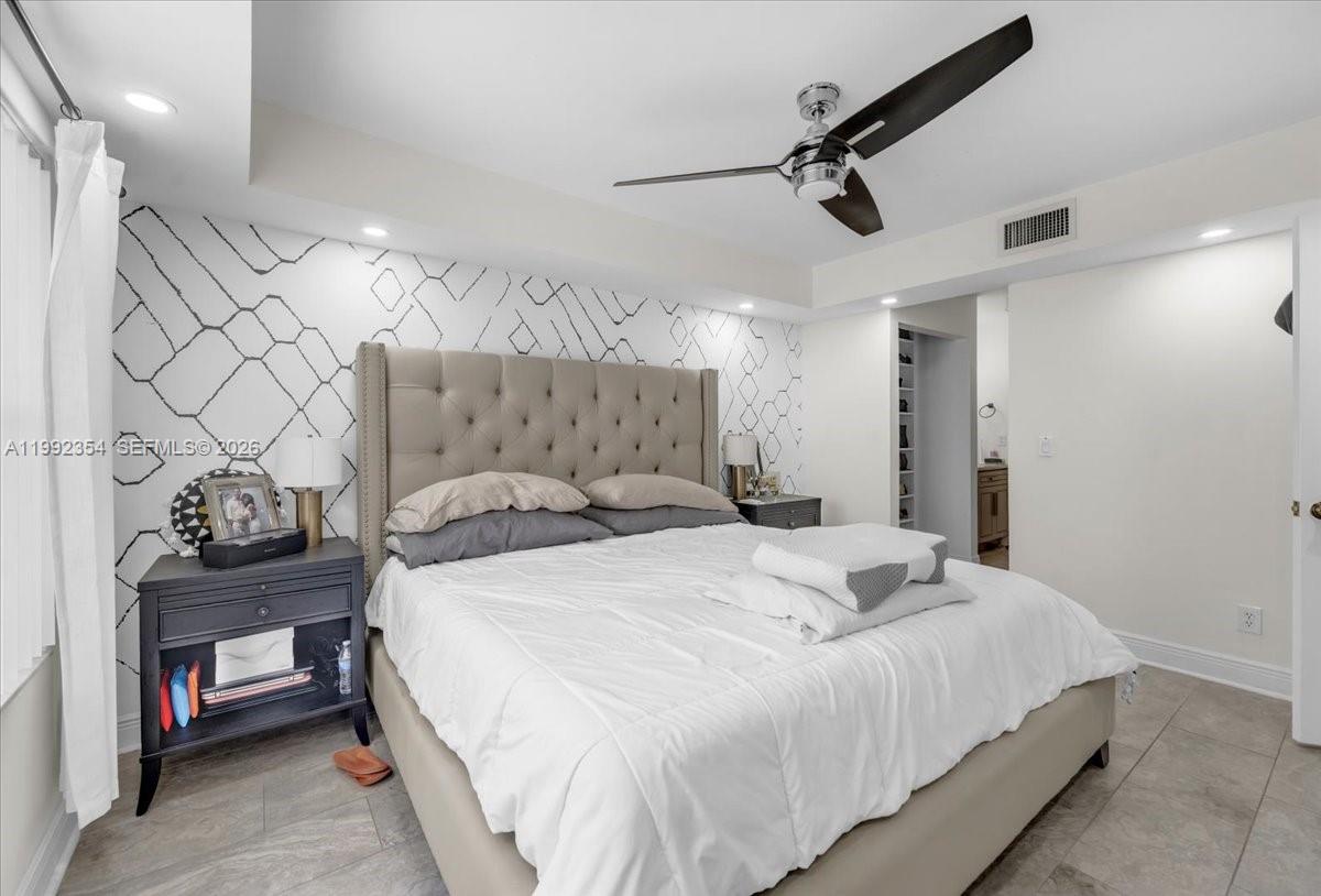 A bedroom features a tufted headboard, geometric wallpaper, a ceiling fan, and tile flooring — 101 Lincoln Ct # 101, Deerfield Beach FL 33442, DEERFIELD BEACH, FL
