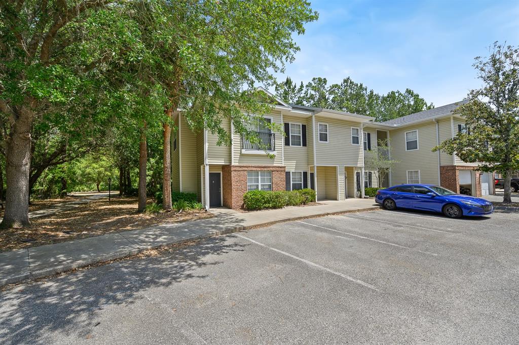 A two-story apartment building with beige siding and a parking lot in the foreground — 5062 NW 44TH LANE UNIT 102, GAINESVILLE, FL