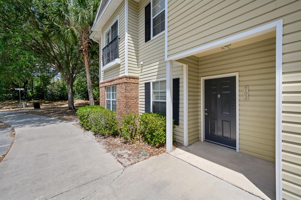 A two-story building with light yellow siding, a dark front door, and a concrete walkway — 5062 NW 44TH LANE UNIT 102, GAINESVILLE, FL