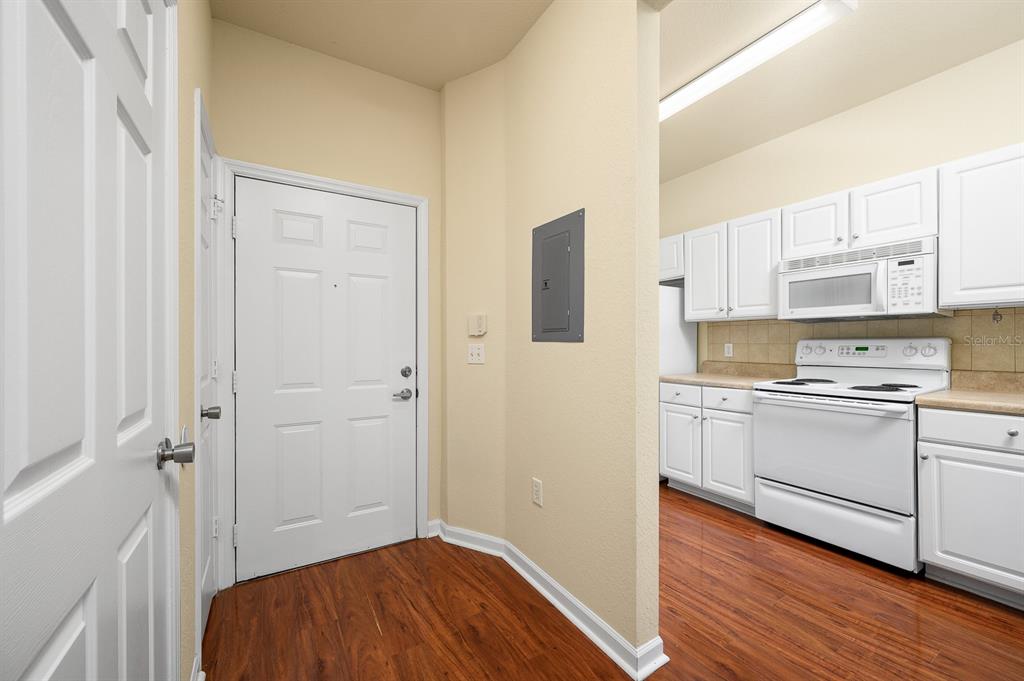 An entryway with wood-look flooring leads into a kitchen featuring white cabinets and appliances — 5062 NW 44TH LANE UNIT 102, GAINESVILLE, FL