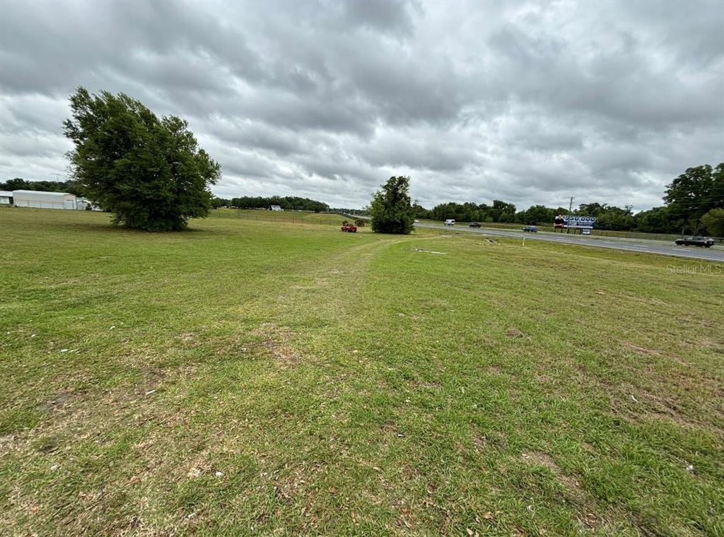 A grassy, open lot sits adjacent to a road with trees and a distant building — TBT SE HWY 484 HIGHWAY SE, BELLEVIEW, FL
